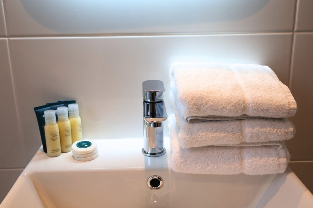 A modern sink with a chrome faucet, three stacked white towels, toiletries, and a round soap bar placed on the basin—perfect touches for a comfortable triple room Dublin stay.