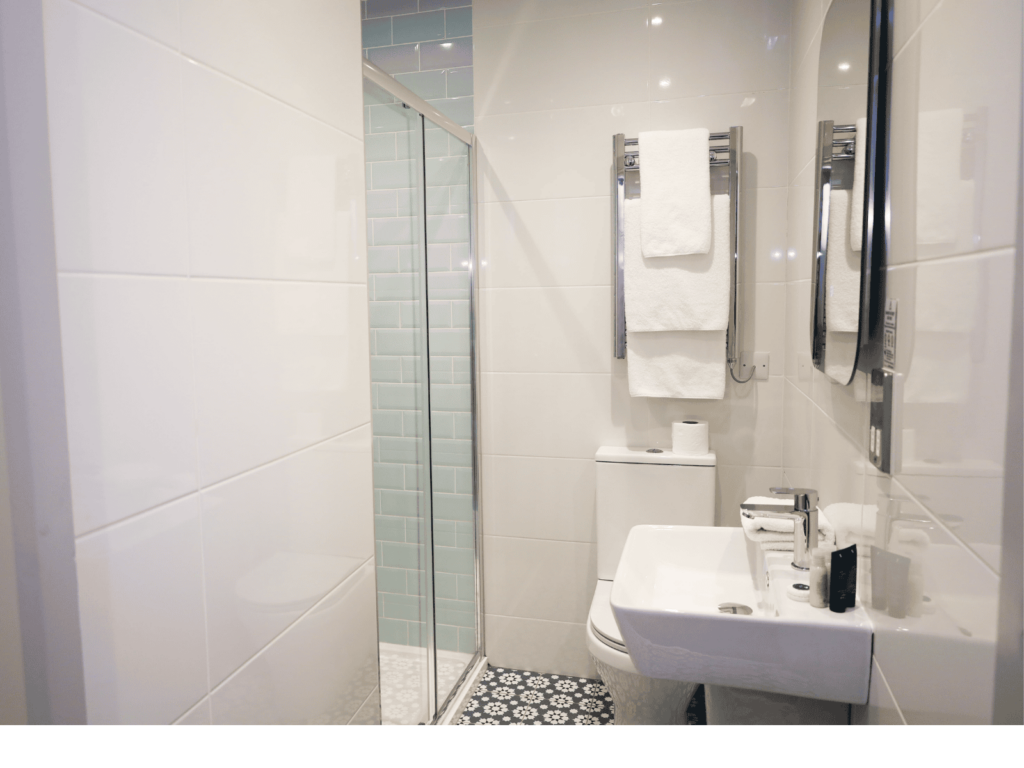 Modern bathroom with a glass-enclosed shower, a white sink, a toilet, patterned floor tiles, and towels on a wall-mounted rack.