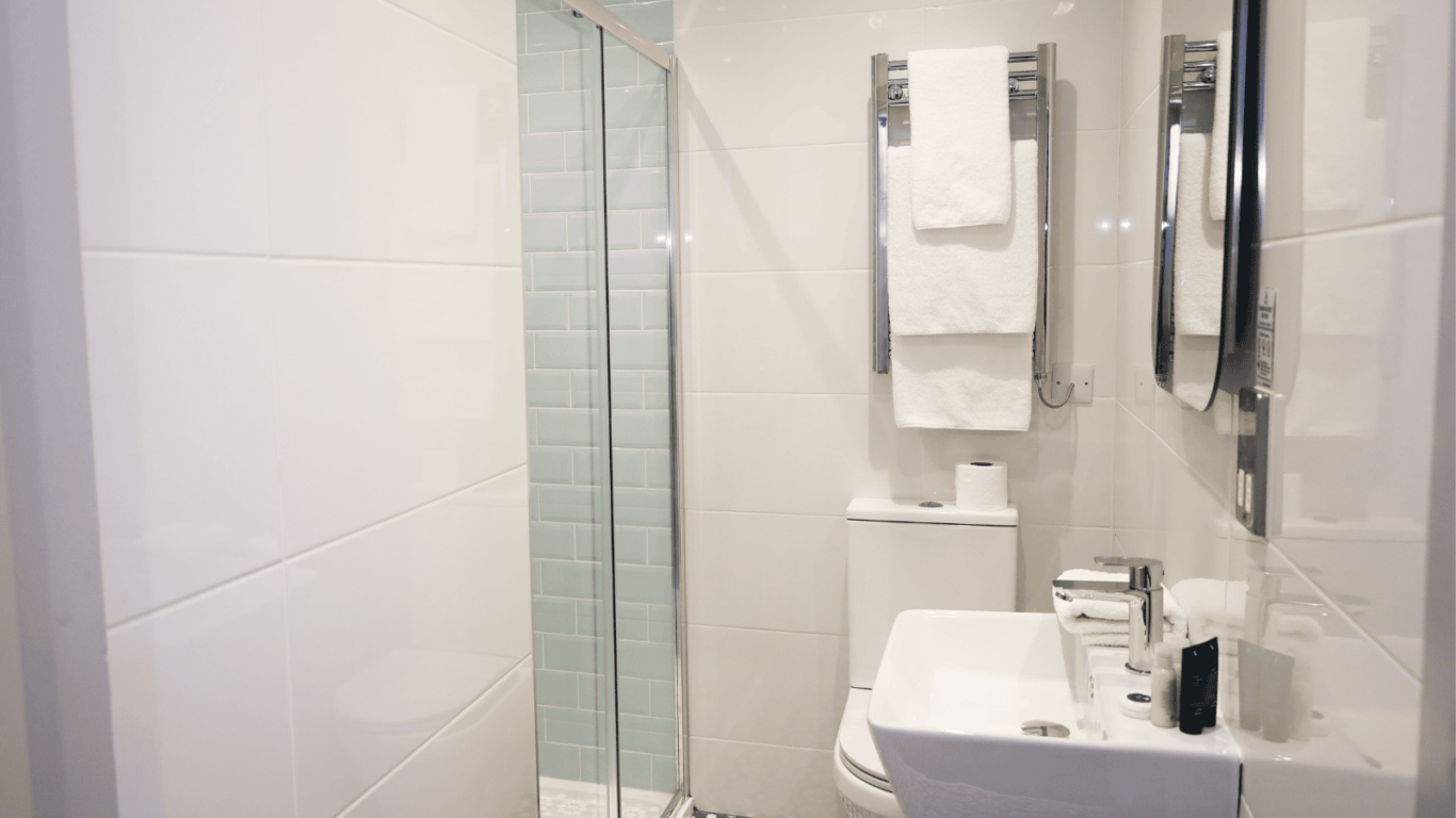 Modern bathroom with a glass-enclosed shower, a white sink, a toilet, patterned floor tiles, and towels on a wall-mounted rack.