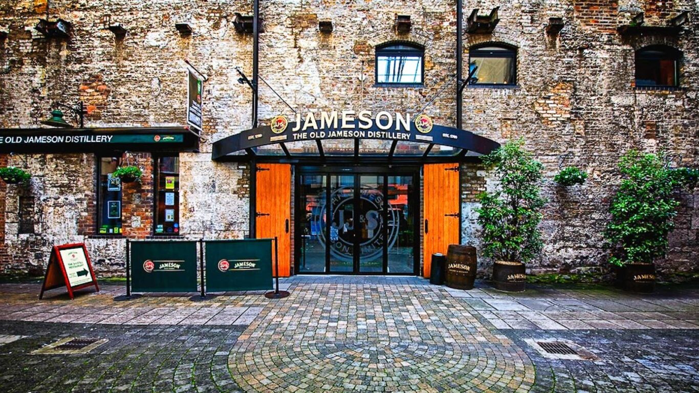 Entrance to the Old Jameson Distillery with glass doors, a Jameson sign above, and a cobbled street in front&mdash;a must-see and one of the Best Things to do in Dublin.