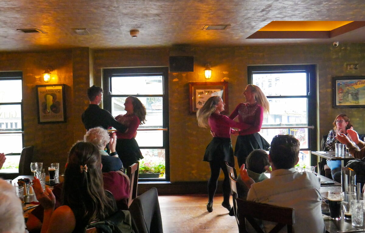 Guests enjoy vibrant Irish dance in cosy pub setting, surrounded by warm lighting and lively atmosphere.