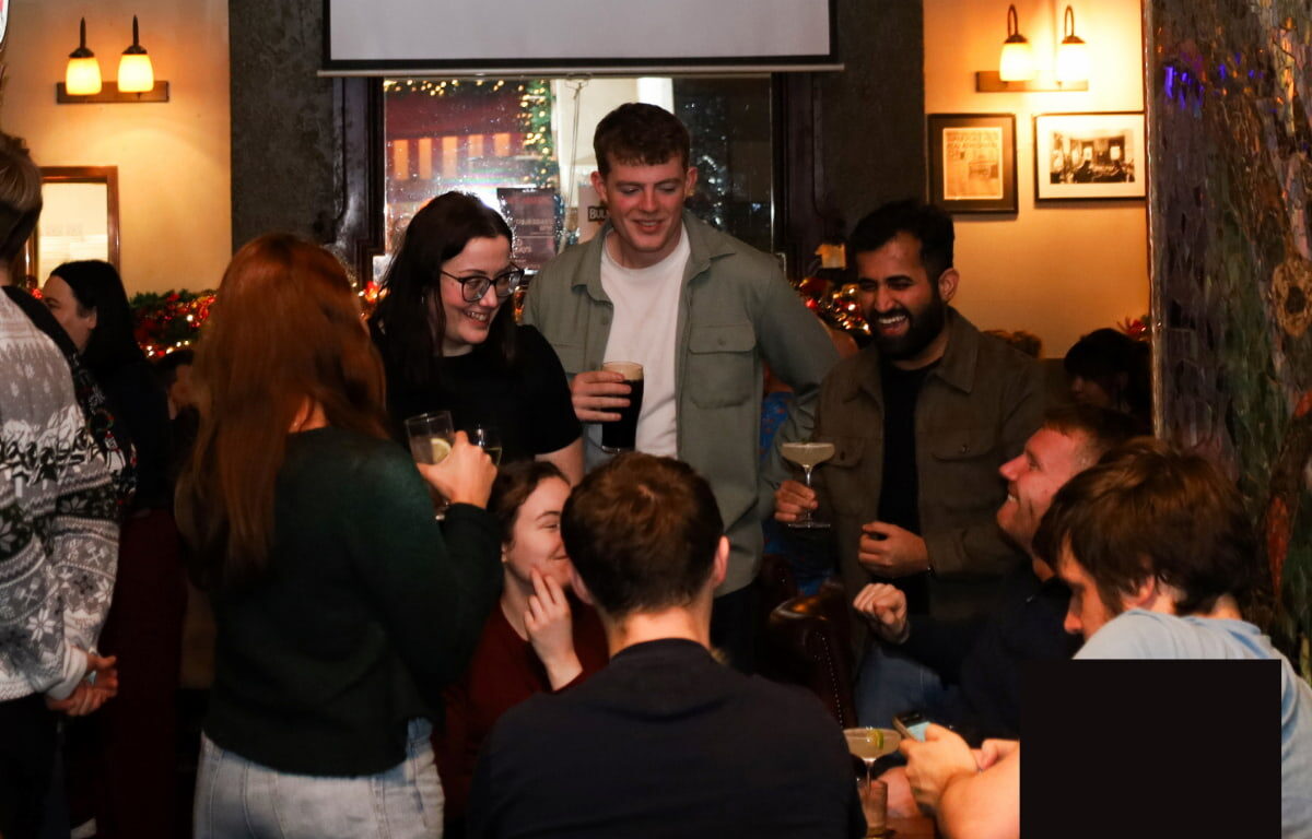 Guests enjoying drinks and laughter in a cosy hotel bar with warm lighting and festive decor, creating a welcoming atmosphere.