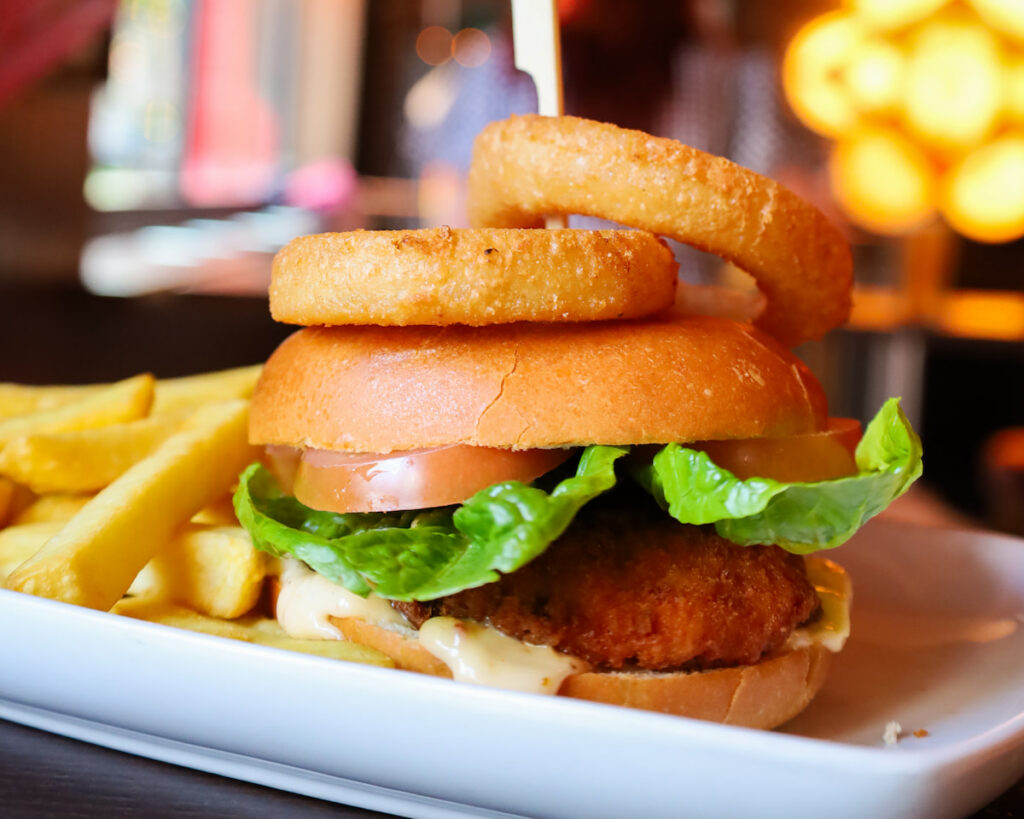 Delicious gourmet burger with crispy onion rings and golden fries in a stylish hotel restaurant setting.