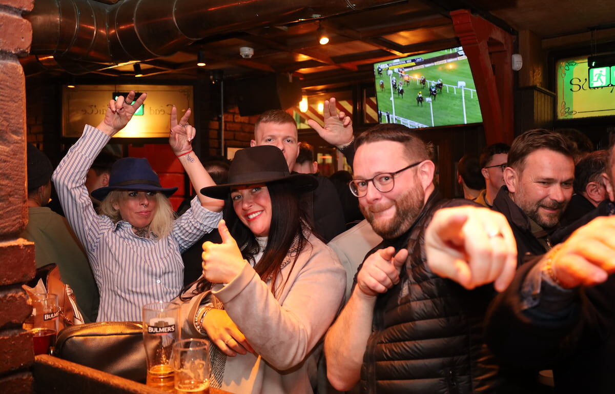 Guests enjoy a lively evening at the hotel bar, with a large screen displaying a horse race, creating a vibrant atmosphere.